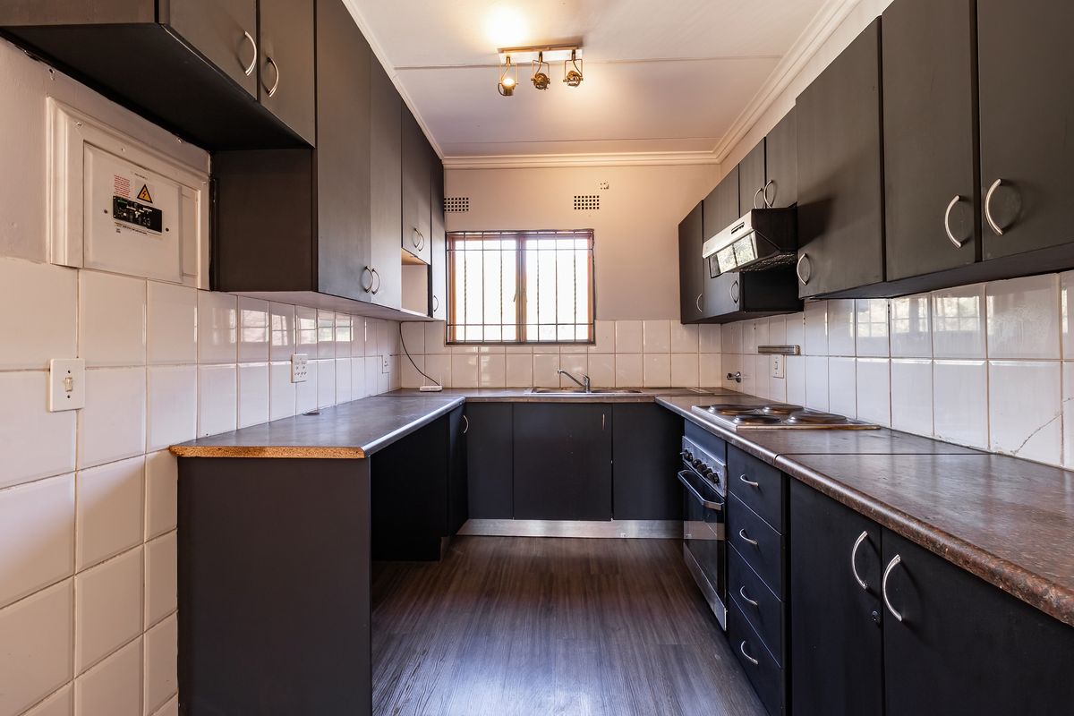 A functional galley-style kitchen featuring dark cabinetry, laminate countertops, built-in oven and hob, and tiled splashbacks.