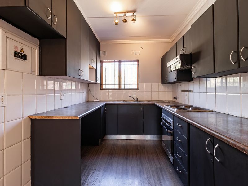 A functional galley-style kitchen featuring dark cabinetry, laminate countertops, built-in oven and hob, and tiled splashbacks.