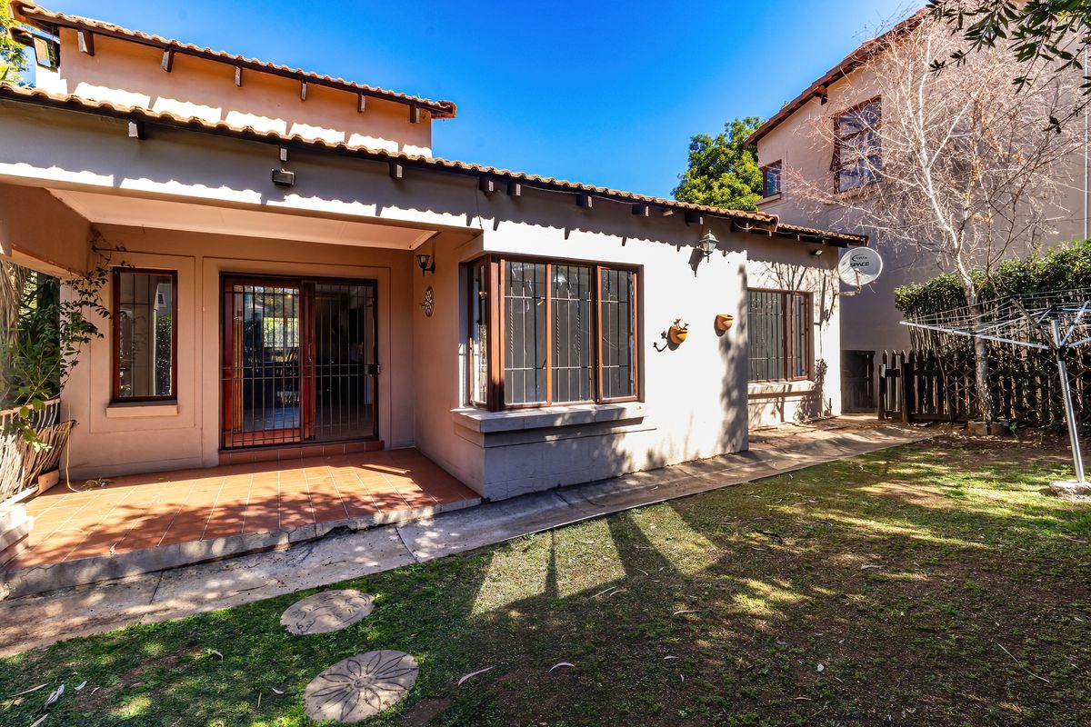 Rear view of the house featuring a covered tiled patio, bay window, and a private garden area with established landscaping.