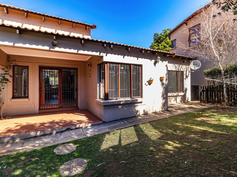 Rear view of the house featuring a covered tiled patio, bay window, and a private garden area with established landscaping.
