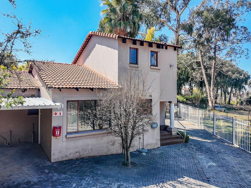 Front exterior view of a two-story house featuring a paved driveway, covered carport, and secure perimeter fencing.
