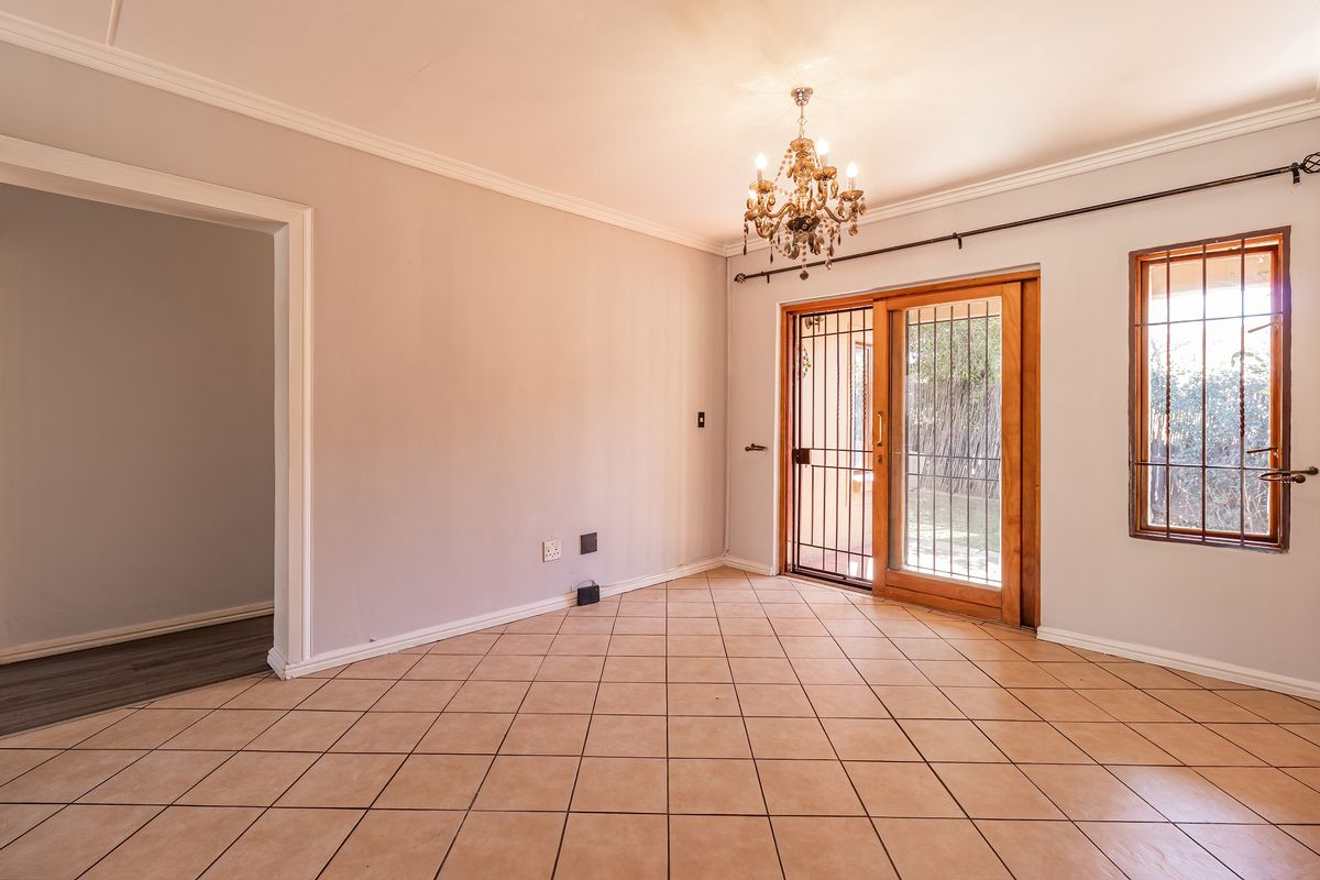 An empty living room featuring tiled flooring, a chandelier, and a sliding glass door with security bars leading to the exterior.