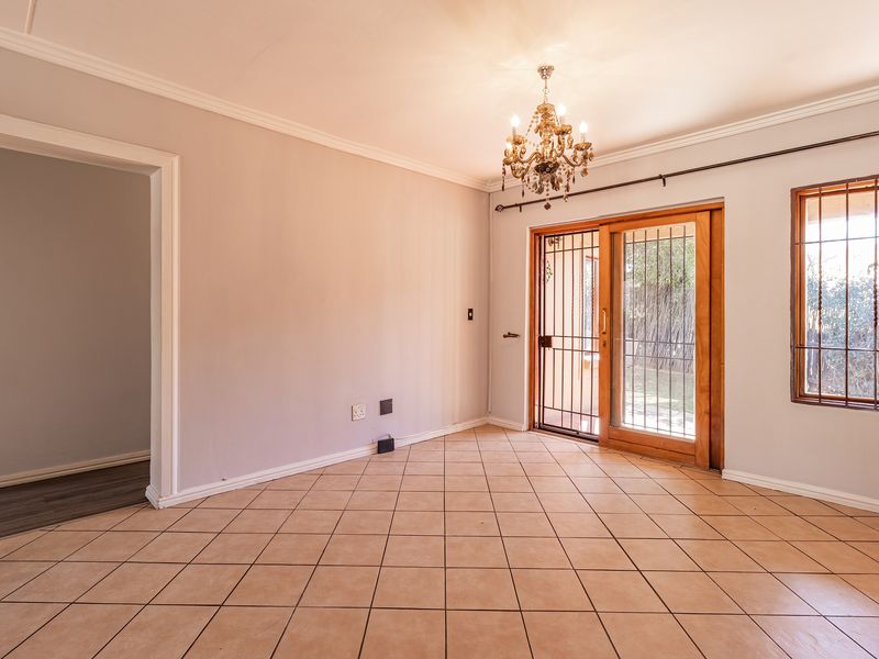 An empty living room featuring tiled flooring, a chandelier, and a sliding glass door with security bars leading to the exterior.