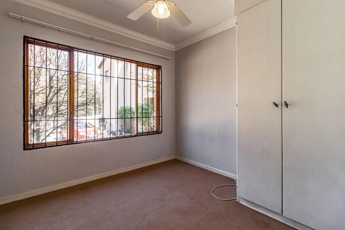 A vacant bedroom featuring built-in wardrobes, carpeted flooring, a ceiling fan, and large windows fitted with security bars.