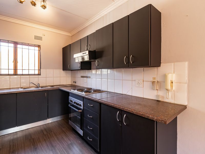 A functional kitchen featuring dark cabinetry, laminate countertops, built-in oven and hob, and a tiled backsplash with a window providing natural light.