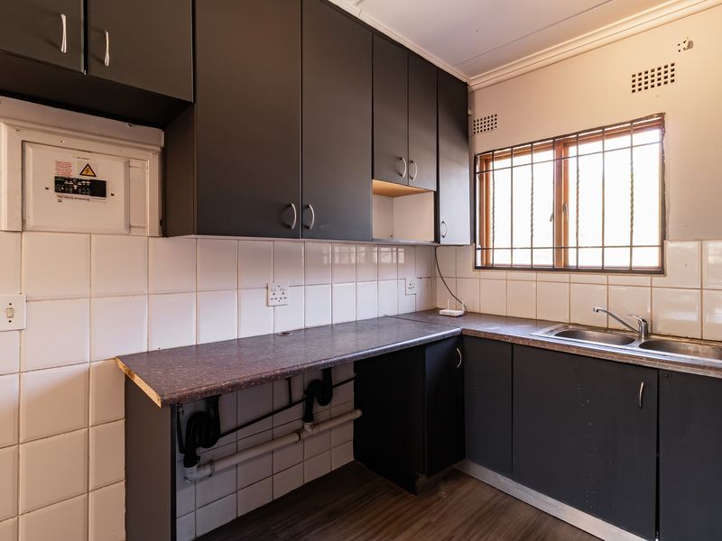 A functional kitchen space featuring dark grey cabinetry, a stainless steel sink, and tiled splashbacks, currently awaiting cosmetic updates and finishing touches.