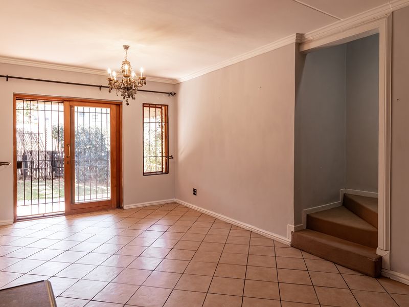An empty living room featuring tiled flooring, crown molding, a chandelier, and a sliding glass door with security gate leading to the exterior.