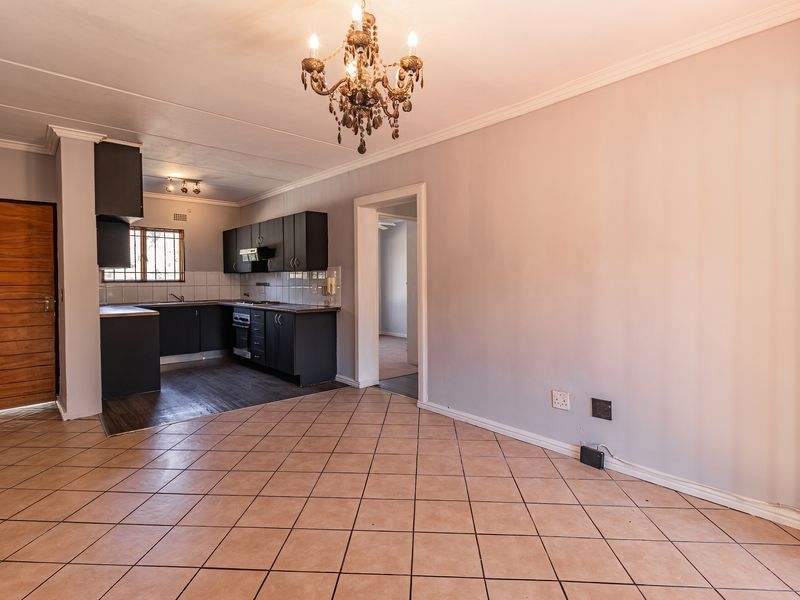 Open-plan living area featuring tiled floors and a functional kitchen with built-in cabinetry, oven, and hob, offering a versatile space for living and dining.