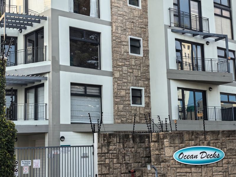Front elevation of the Ocean Decks apartment complex featuring stone cladding, secure gated access, electric fencing, and multiple private balconies.