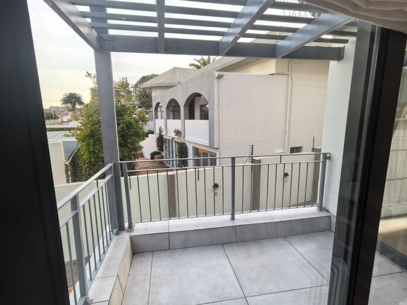 A clean, modern balcony featuring a metal pergola structure, tiled flooring, and metal safety railings, offering an open outdoor space.