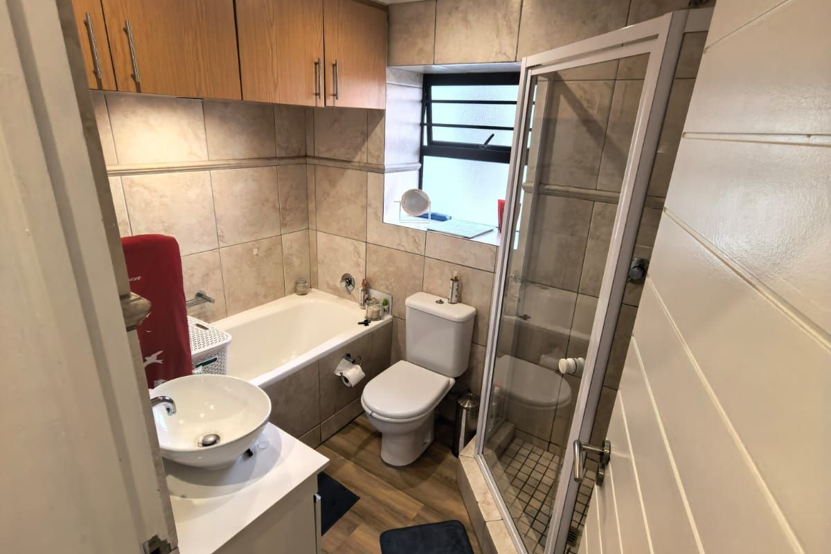 A functional bathroom featuring a separate bathtub and shower enclosure, vanity with vessel sink, and wall-mounted storage cabinetry with neutral tiled finishes.