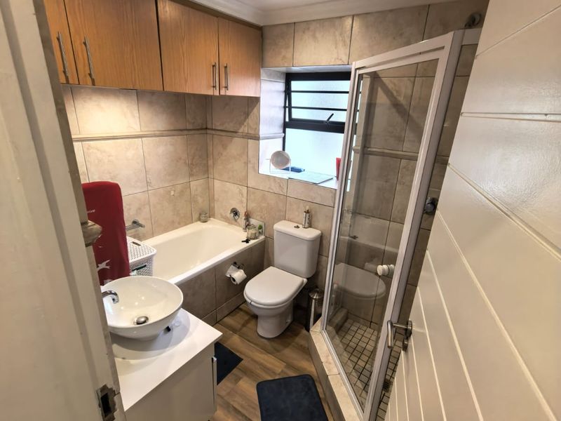 A functional bathroom featuring a separate bathtub and shower enclosure, vanity with vessel sink, and wall-mounted storage cabinetry with neutral tiled finishes.