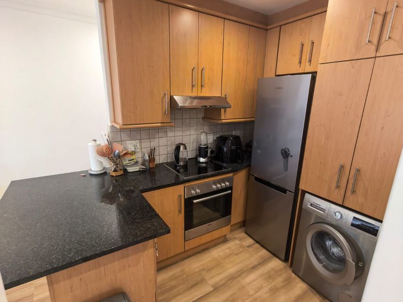 A functional kitchen featuring light wood cabinetry, dark granite countertops, a tiled backsplash, and integrated appliances including an oven and hob.