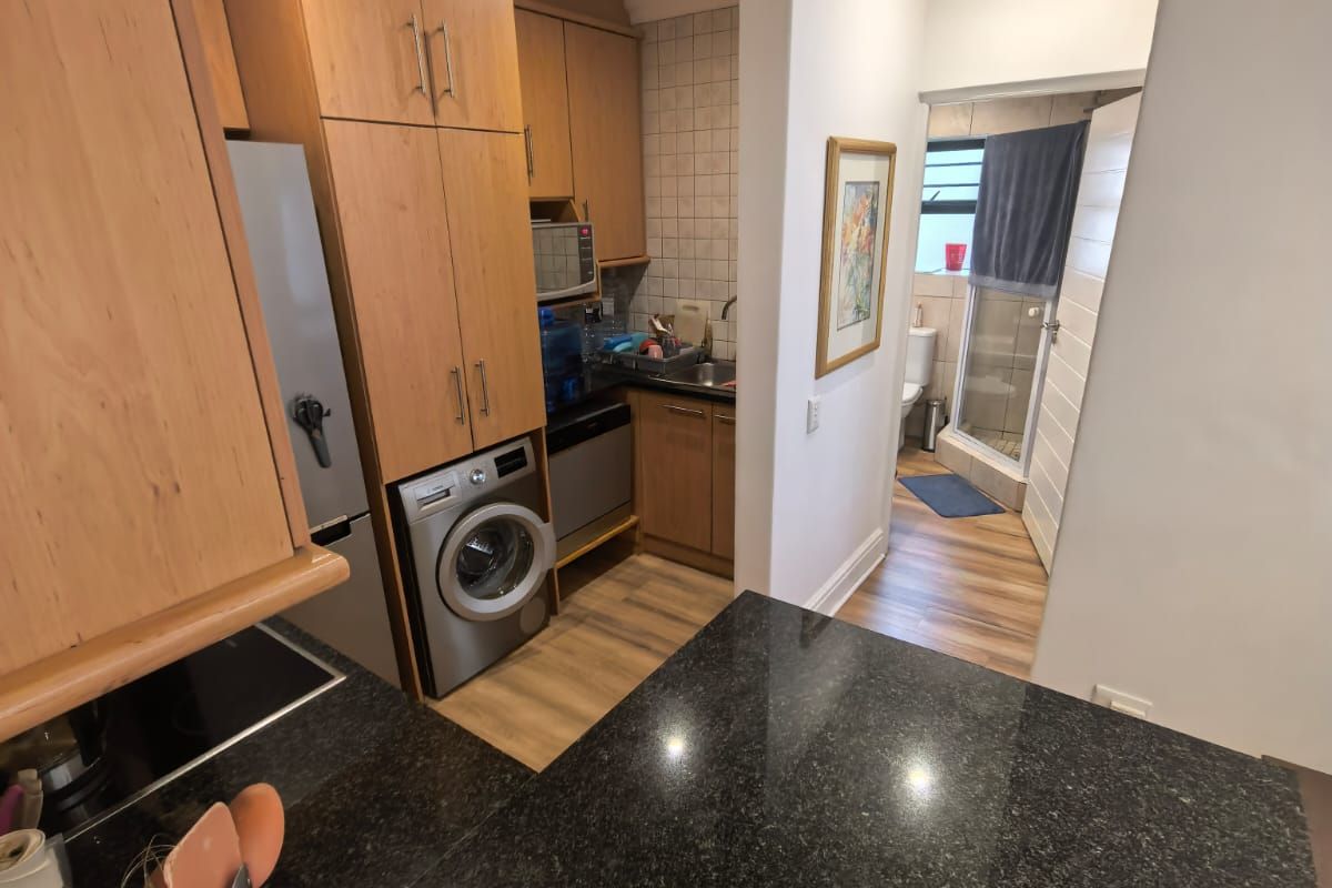 Compact kitchen featuring granite countertops, wood-finish cabinetry, and integrated laundry appliances, with an adjacent view into a small bathroom area.