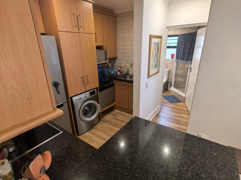 Compact kitchen featuring granite countertops, wood-finish cabinetry, and integrated laundry appliances, with an adjacent view into a small bathroom area.