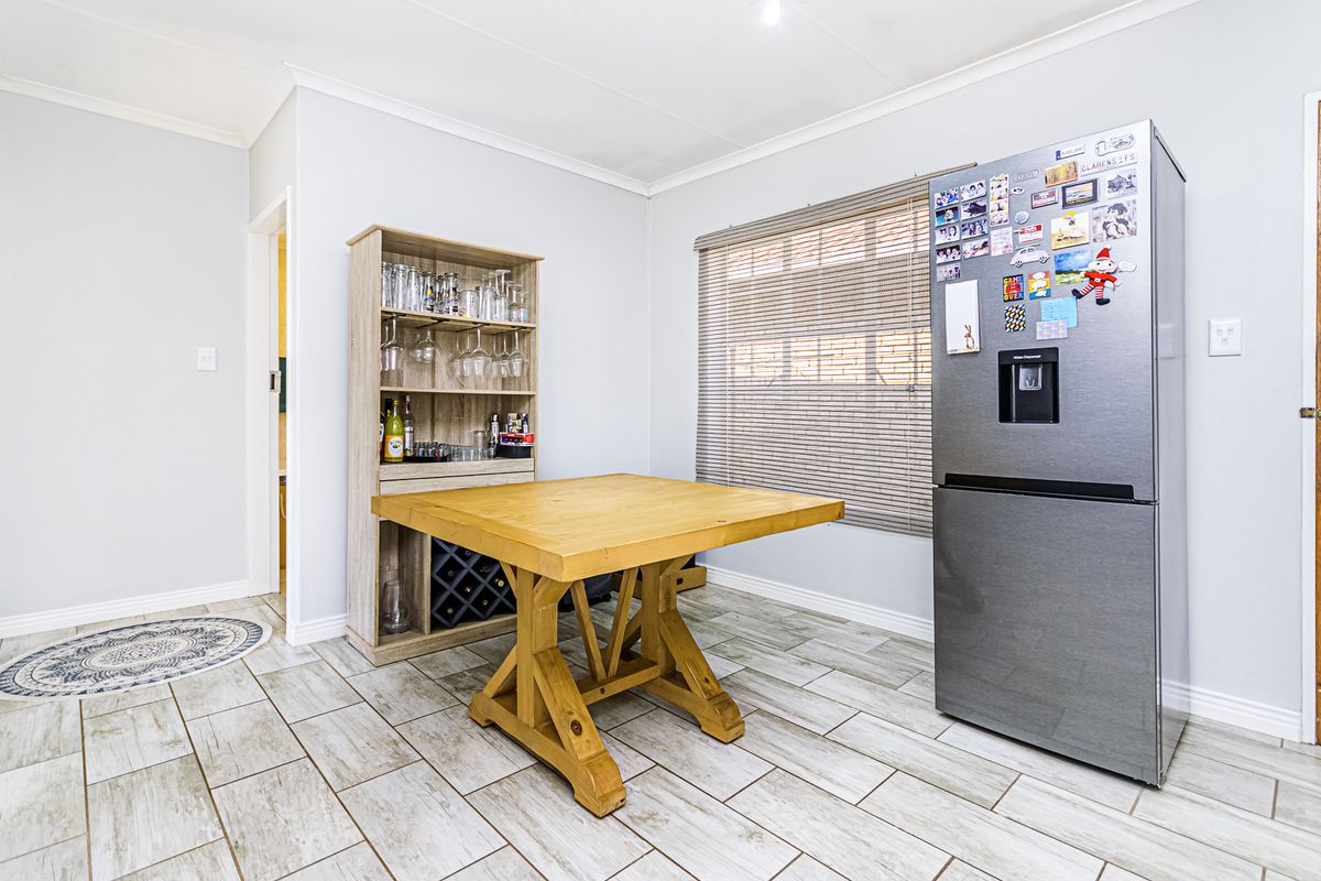 A bright kitchen area featuring light-toned tiled flooring, a coved ceiling, and a window fitted with a roller blind.