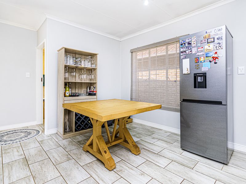 A bright kitchen area featuring light-toned tiled flooring, a coved ceiling, and a window fitted with a roller blind.