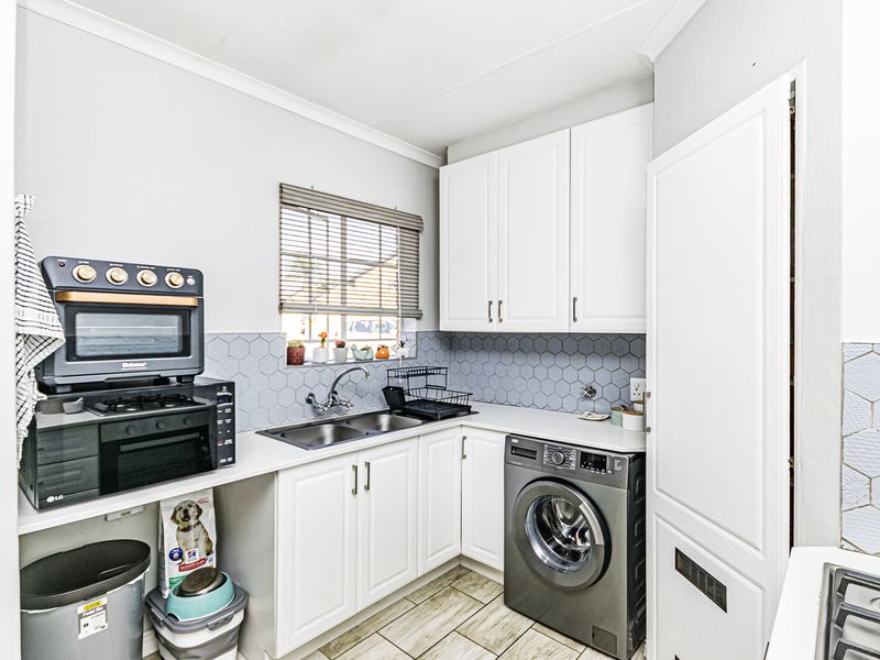 A functional scullery featuring white cabinetry, a double basin sink, hexagon tile backsplash, and dedicated space for laundry appliances.