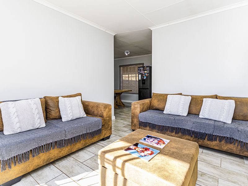 A bright living room featuring neutral walls, tiled flooring, and coved ceilings, with an open transition leading into the adjacent kitchen area.