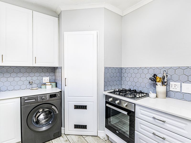 A well-maintained kitchen featuring white cabinetry, a gas hob, built-in oven, and stylish blue hexagonal tile backsplash with integrated laundry space.