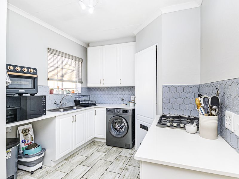 A functional kitchen featuring white cabinetry, a gas hob, double sink, and modern hexagonal tiled backsplash with light-toned tiled flooring.