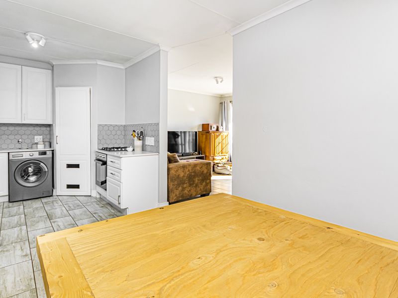 Open plan kitchen area featuring modern white cabinetry, hexagonal tile backsplash, and integrated appliances, flowing into the adjacent living space.