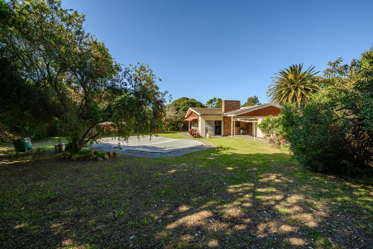 Rear view of the property featuring a swimming pool with cover, a covered patio area, and a spacious garden with mature trees.