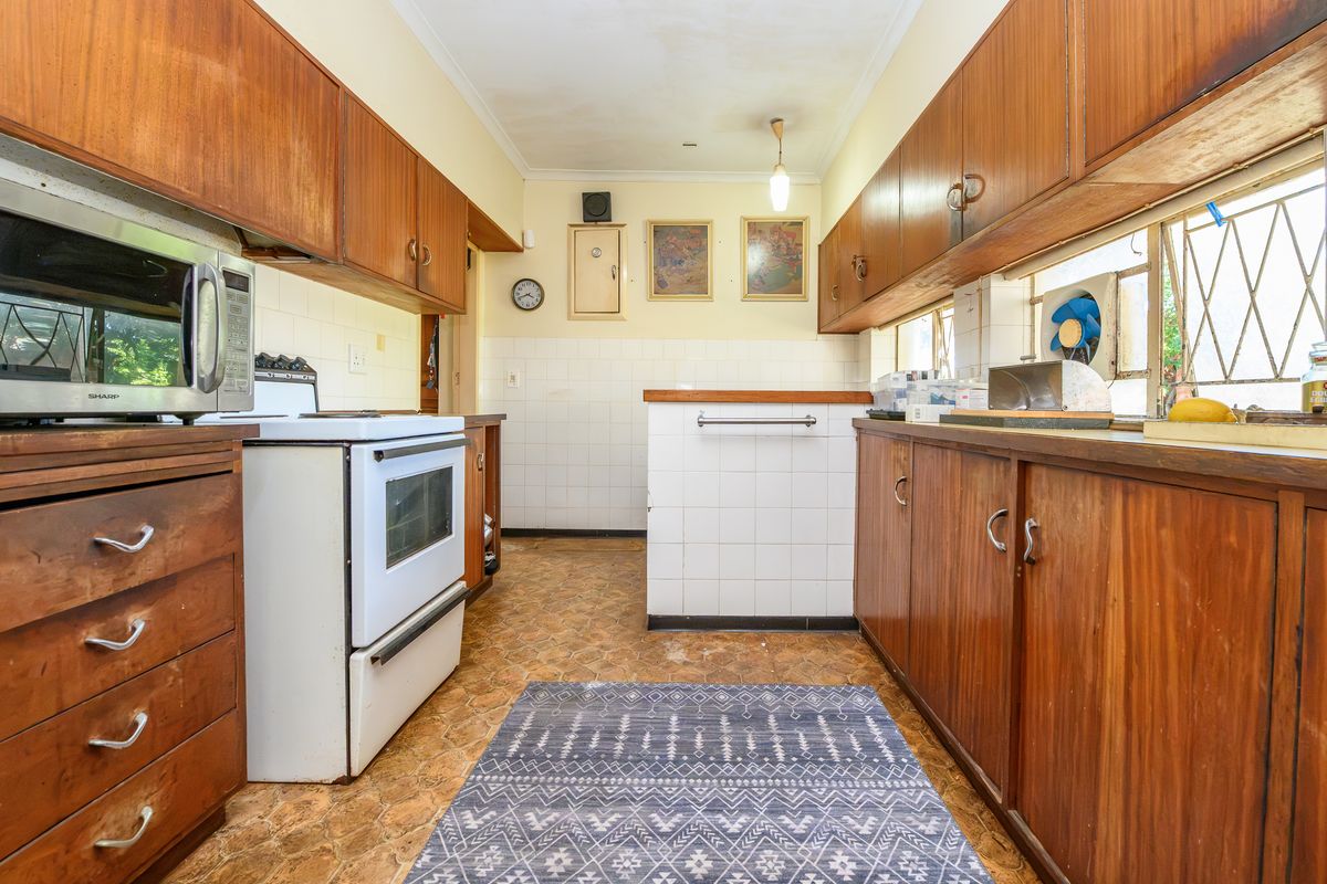 A dated kitchen featuring original wooden cabinetry, tiled backsplash, and a freestanding oven, offering significant potential for a modern renovation.