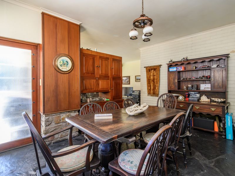 A dining room featuring a stone fireplace, wood paneling, painted brick walls, and slate flooring, with direct access to the exterior via a glass door.