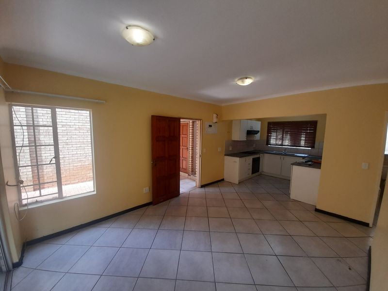 An open-plan living and kitchen area featuring tiled flooring, built-in cabinetry, and integrated kitchen appliances in a neutral, well-lit space.