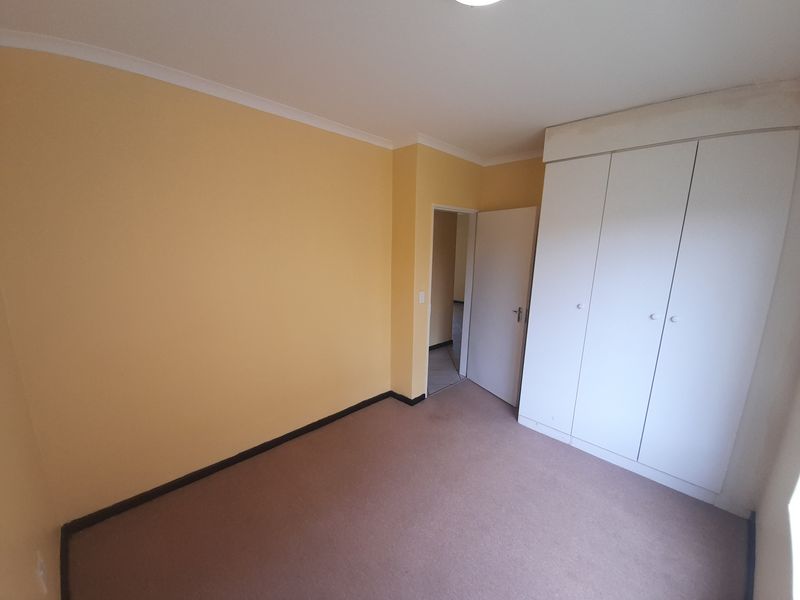 A clean, empty bedroom featuring neutral yellow walls, fitted white built-in cupboards, and carpeted flooring.