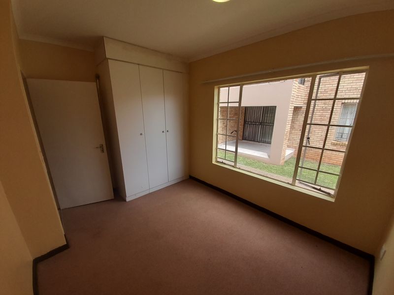 A vacant bedroom featuring a built-in wardrobe, carpeted flooring, and a large window overlooking the exterior grounds.