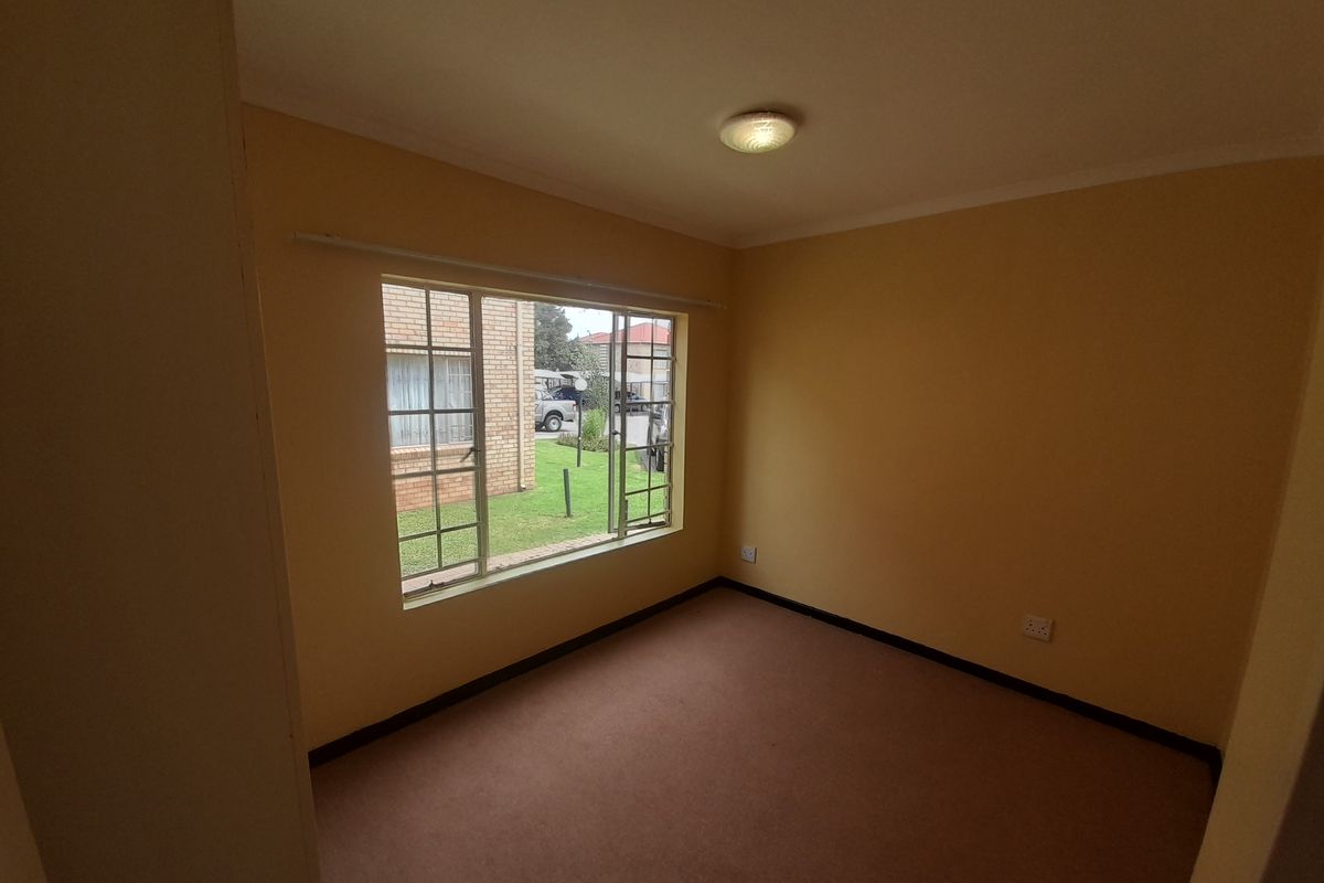 An empty bedroom featuring carpet flooring, neutral walls, and a large metal-framed window providing natural light and views of the exterior grounds.
