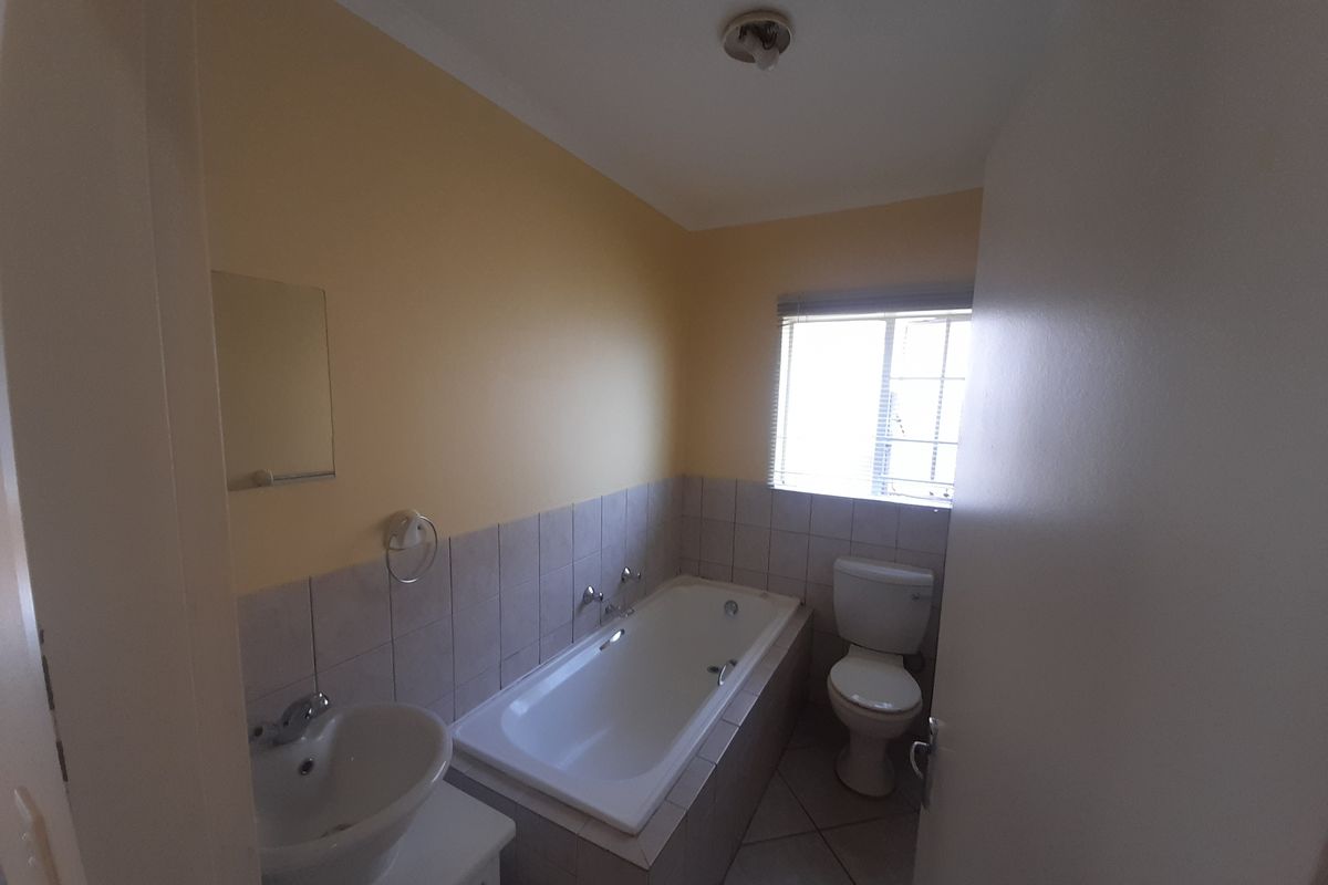 A functional bathroom featuring a built-in bathtub, pedestal basin, and toilet, finished with neutral wall and floor tiling.
