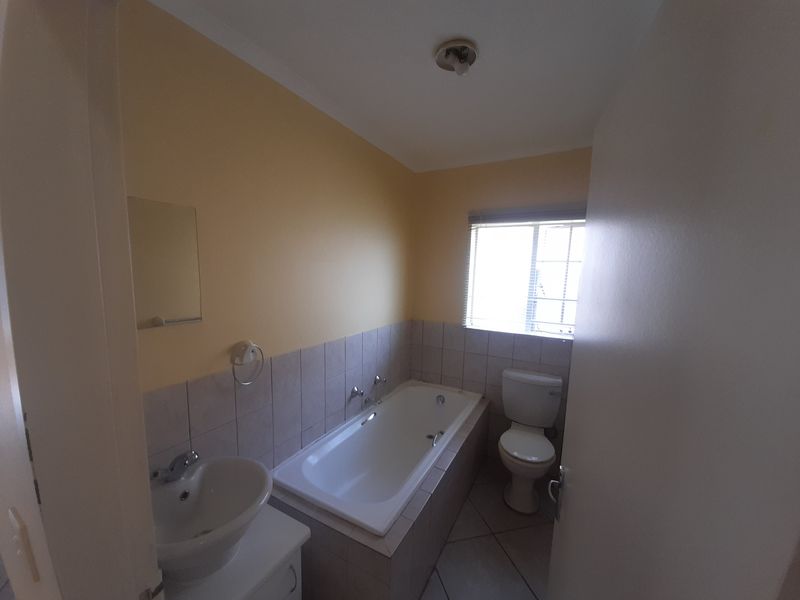 A functional bathroom featuring a built-in bathtub, pedestal basin, and toilet, finished with neutral wall and floor tiling.