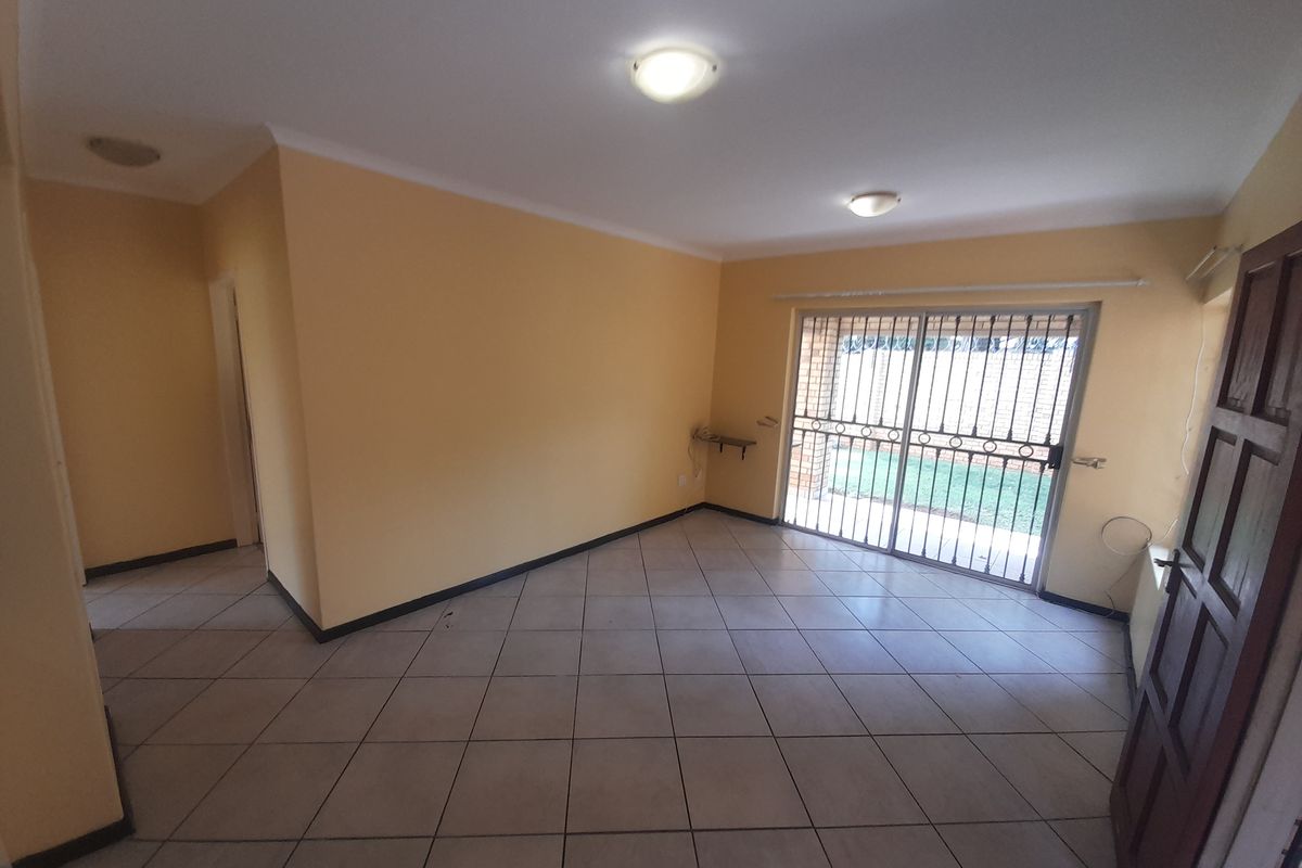 An empty, open-plan living area featuring neutral tiled flooring, yellow walls, and a sliding glass door with a security gate leading to the exterior.
