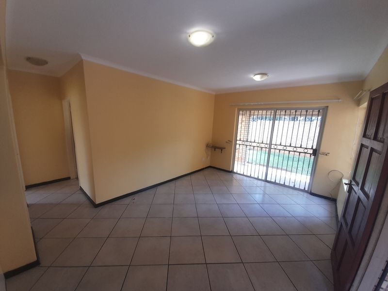 An empty, open-plan living area featuring neutral tiled flooring, yellow walls, and a sliding glass door with a security gate leading to the exterior.