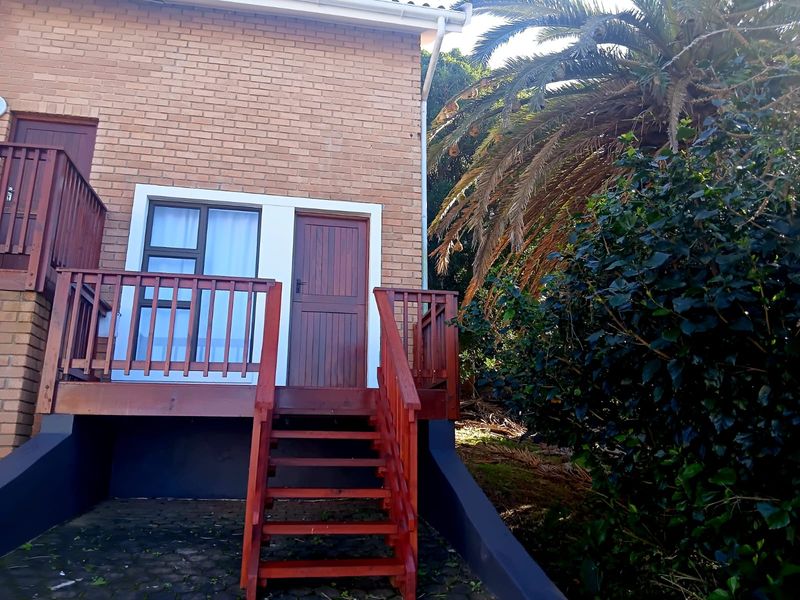 Rear exterior view of the cottage featuring a raised timber deck, staircase, and brick facade with access door and window.