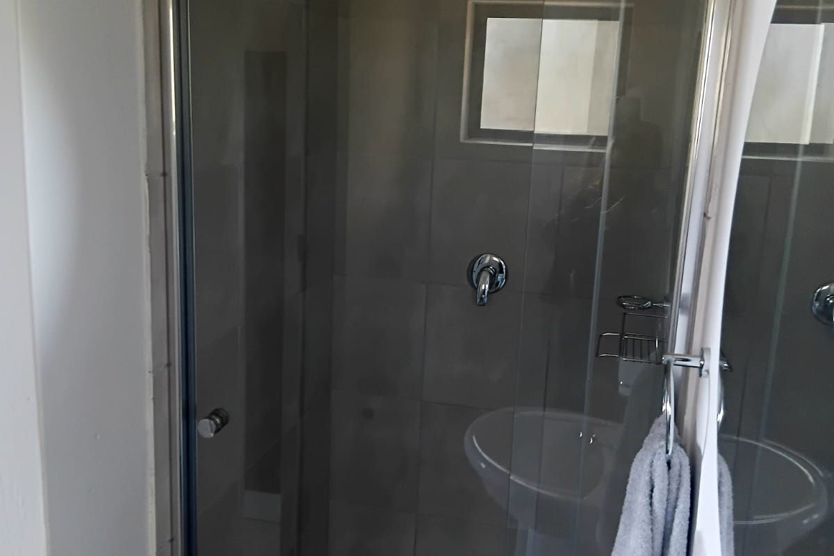 A functional bathroom featuring a glass-enclosed shower with tiled walls and a pedestal basin.