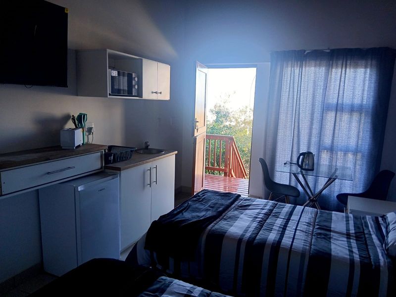 Compact open-plan studio cottage featuring a kitchenette with built-in cabinetry and microwave, leading directly onto a private timber deck.