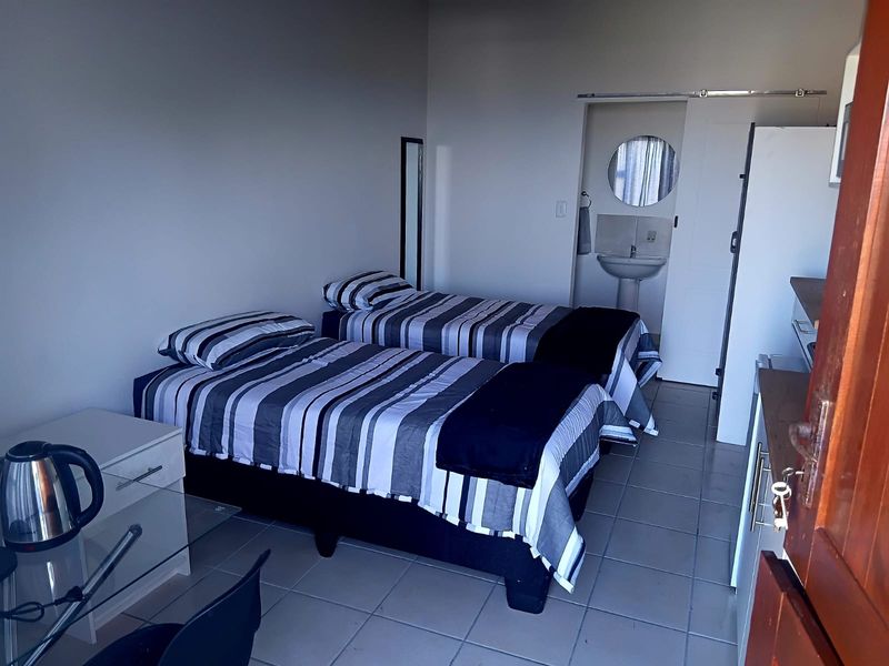 A functional bedroom featuring tiled flooring and an en-suite area with a pedestal basin and sliding door access.