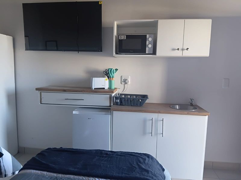 Compact kitchenette area featuring white cabinetry, a small sink, built-in microwave, and wooden countertop, integrated into a living or bedroom space.