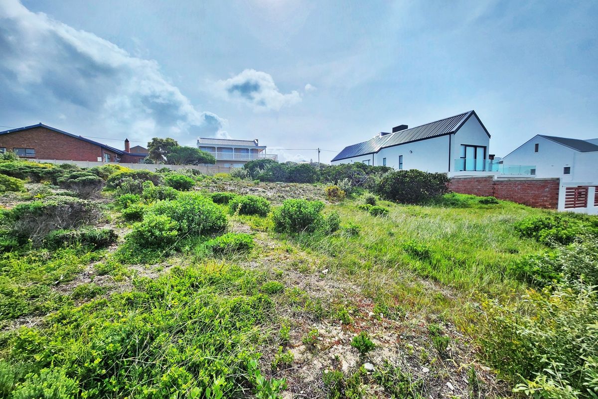 A view of a vacant residential plot featuring natural coastal vegetation and surrounding residential properties.