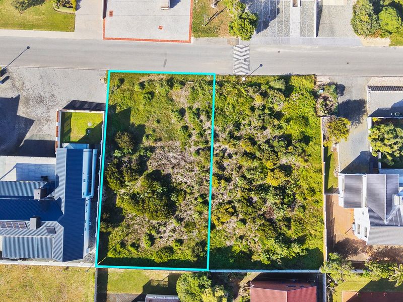 An aerial view of a vacant residential plot situated between existing homes, featuring natural vegetation and clear boundary lines.