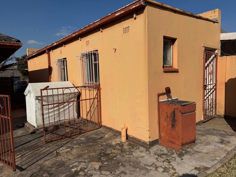 Rear exterior view of the property featuring a weathered facade, security bars on windows, and an external wash basin area with cracked concrete paving.