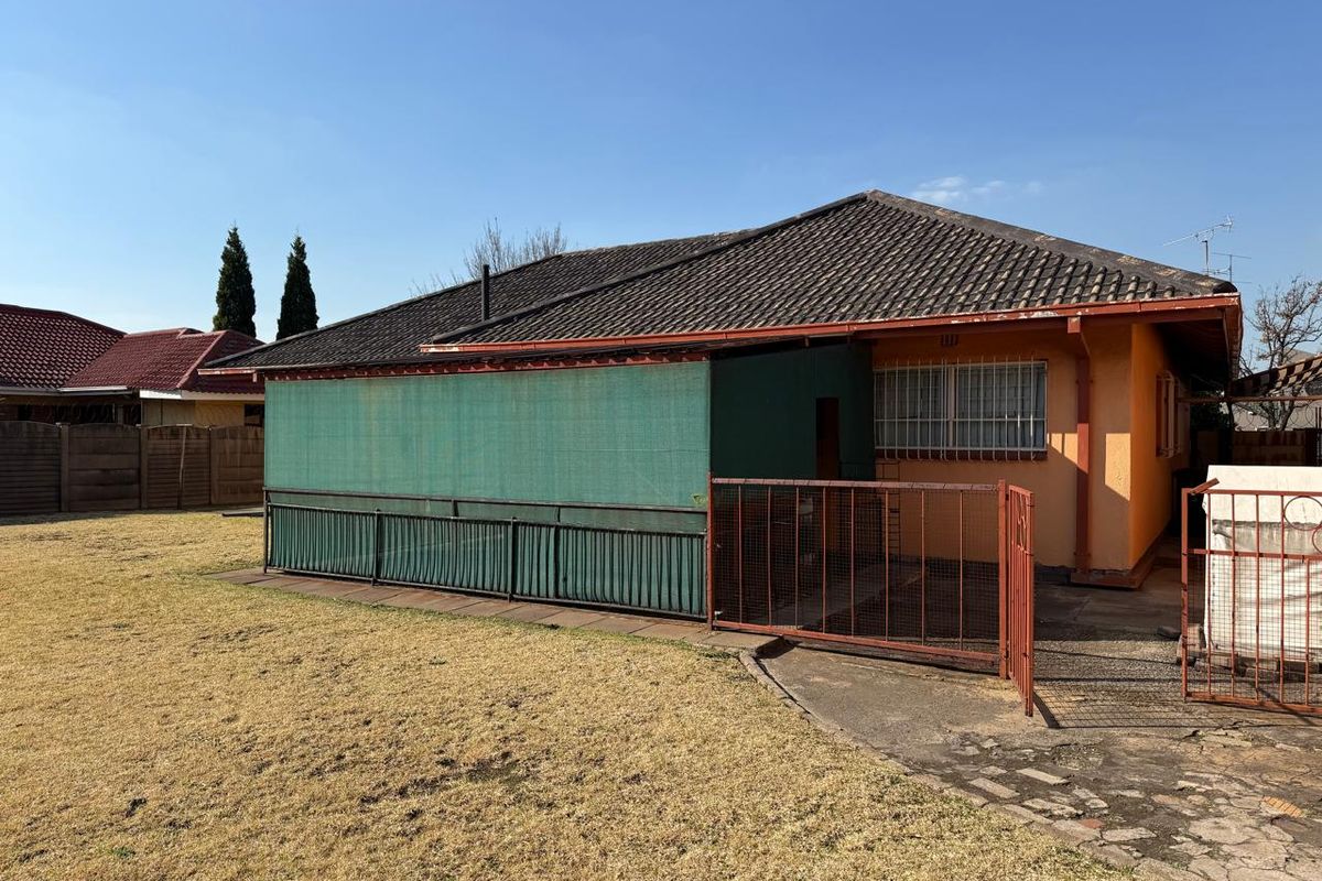 Rear view of the property featuring a tiled roof, security bars on windows, and a paved area enclosed by metal fencing and shade cloth.