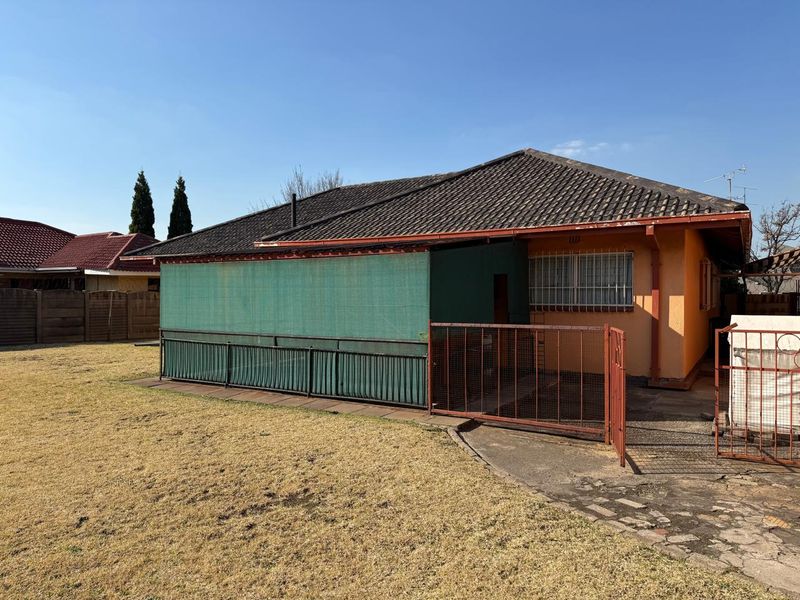 Rear view of the property featuring a tiled roof, security bars on windows, and a paved area enclosed by metal fencing and shade cloth.