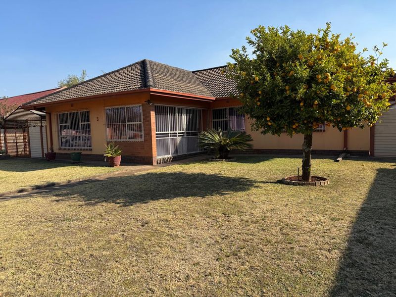 Front view of a single-story brick house featuring a tiled roof, security bars on windows, and a well-maintained garden with a mature fruit tree.
