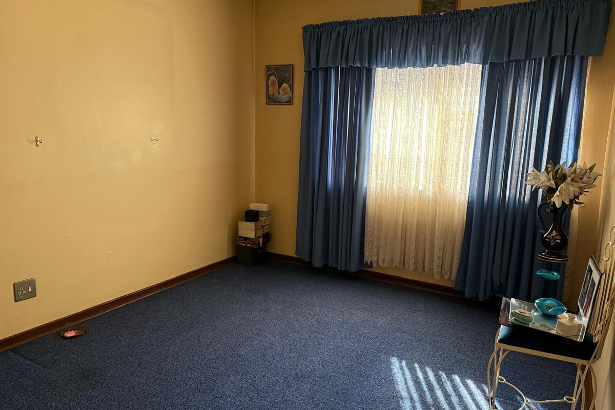 A vacant bedroom featuring blue carpeting and large windows with curtains, requiring cosmetic updates to the walls and ceiling.
