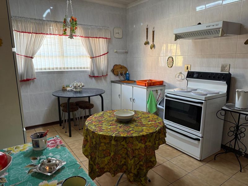 A functional kitchen featuring tiled walls and flooring, equipped with a freestanding stove, extractor fan, and built-in cabinetry.